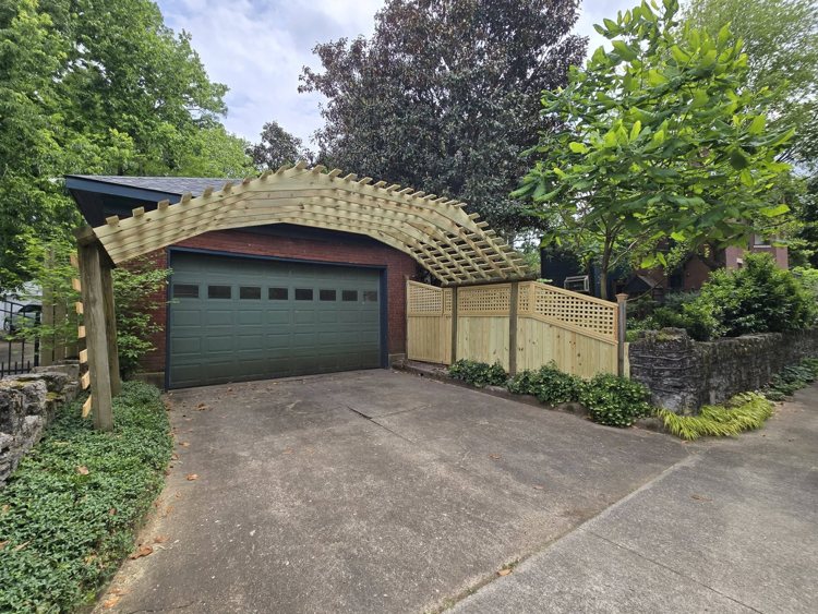 Curved wooden arbor across a garage driveway with an adjoining lattice-top fence